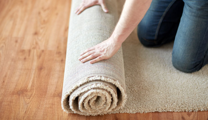 A person rolling out a carpet on wooden floor