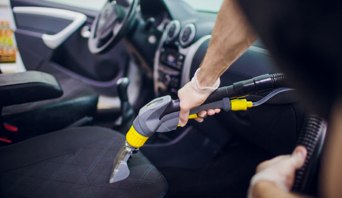 A person is using a vacuum cleaner to clean the interior of a car.