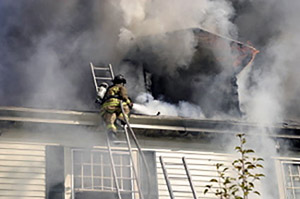 Photo: house on fire with heavy smoke billowing from the roof and windows.